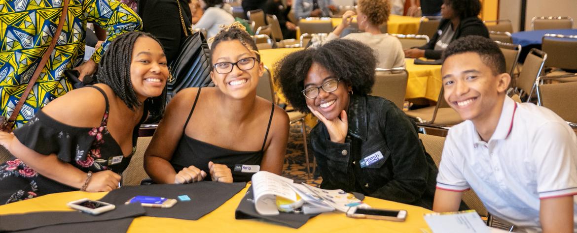 Three female and one male student, formally dressed up sitting at a round table attending Black Excellence event