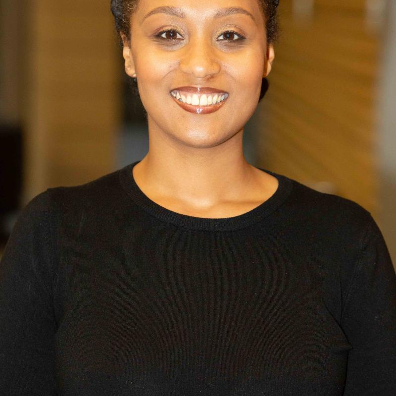 A young Black woman, wearing a black sweater, smiling at the camera