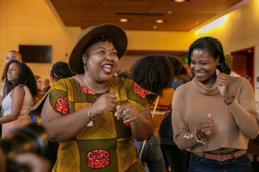 Female participants of Black Excellence event at smiling and dancing in event venue lobby